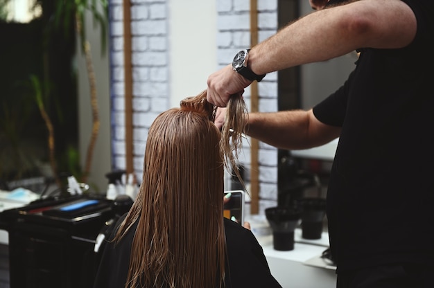 Uma cabeleireira penteando o cabelo comprido e úmido de uma cliente de salão de beleza