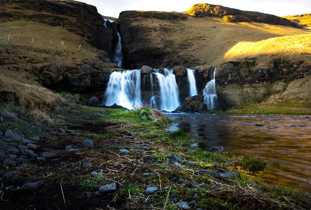 Foto uma cachoeira na islândia com um campo verde em primeiro plano.