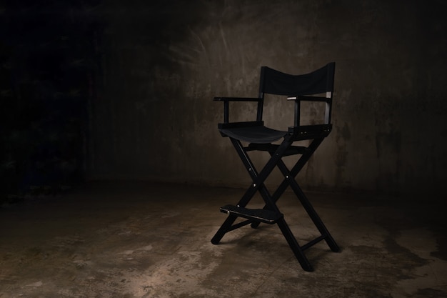 Uma cadeira de madeira preta fica em um estúdio de fotografia no contexto de um muro de concreto velho e arranhado.
