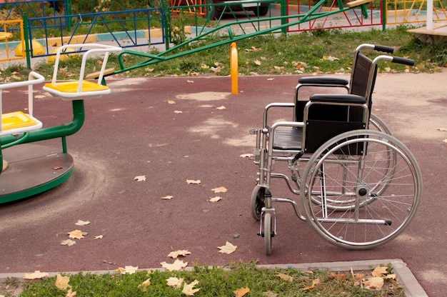 Foto uma cadeira de rodas vazia está parada na rua no asfalto do parquinho infantil no quintal