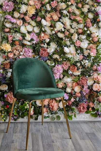 Uma cadeira verde elegante e elegante fica encostada em uma parede decorativa feita de botões de flores multicoloridos
