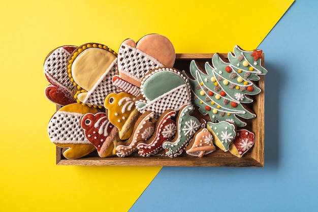 Uma caixa de natal gingerbread em fundo amarelo e azul. floco de neve, pinheiro, luva, abeto, estrela, trenó, cones, cone, estrela, forma de sino.