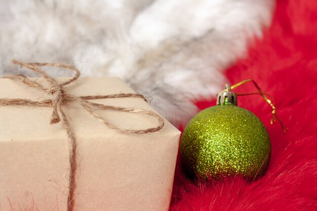 Uma caixa de papel artesanal cinza e uma bola de natal verde em peles brancas e vermelhas macias. no presente é um arco de corda de cânhamo. foco seletivo no presente. copie o espaço.