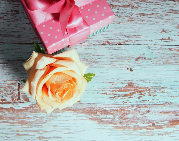 Uma caixa de presente com um laço rosa em um fundo de madeira, cópia do espaço de texto uma rosa nas proximidades.