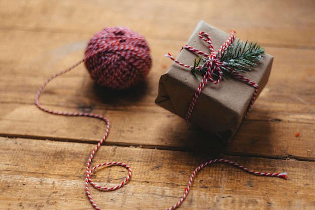 Uma caixa de presente de Natal amarrada com uma fita branca e vermelha em uma mesa rústica de madeira ao lado de uma corda de embalagem Embalagem de presentes de Natal