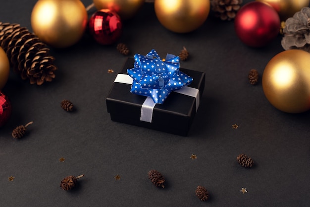 Uma caixinha de presente com uma fita em um fundo escuro entre cones e bolas de Natal