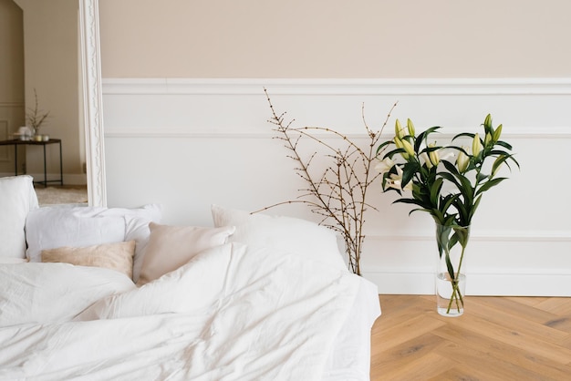 Uma cama aconchegante e brilhante com almofadas e flores de lírio em um vaso de galhos de árvores interior escandinavo