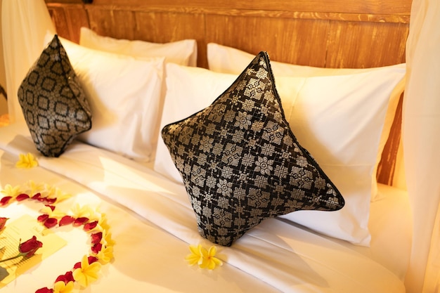 Uma cama com um canteiro de flores e uma cama com um lençol branco e um travesseiro preto com uma flor em cima.