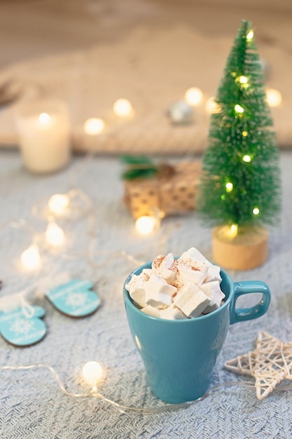 Uma caneca azul com fundo azul de marshmallows de cacau de decoração de Natal fica em uma malha azul