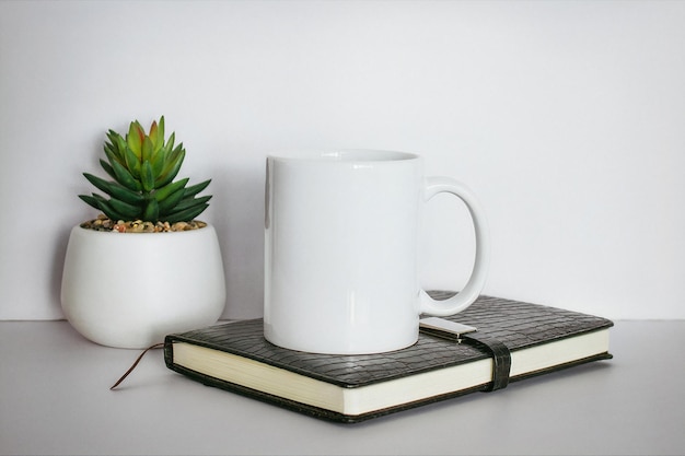 Uma caneca de café branca está sobre um livro sobre uma mesa ao lado de uma planta.