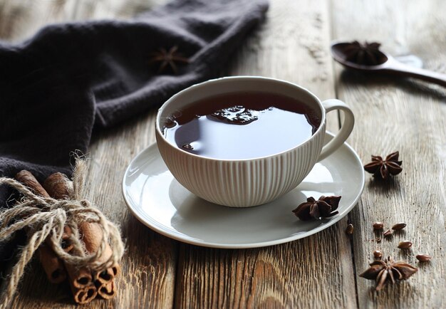 Uma caneca de chá preto está sobre uma mesa de madeira Uma toalha de algodão marrom anis estrelado e paus de canela estão por perto
