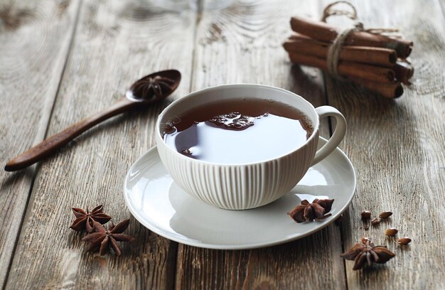 Uma caneca de chá preto fica em uma mesa de madeira Estrelas de anis e paus de canela estão nas proximidades