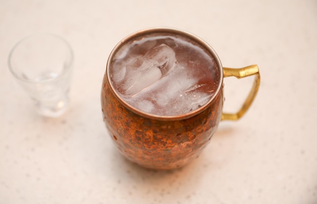 Uma caneca de cobre com uma bebida e um copo de água ao lado.