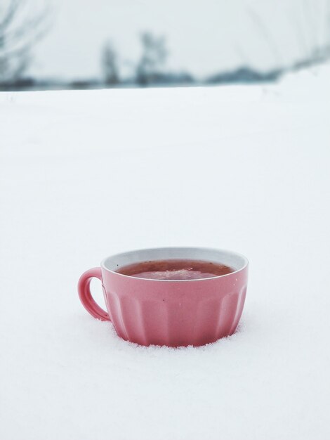 Uma caneca rosa com chá de framboesa quente em um campo de inverno nevado. O chá com geléia aquece no inverno frio.