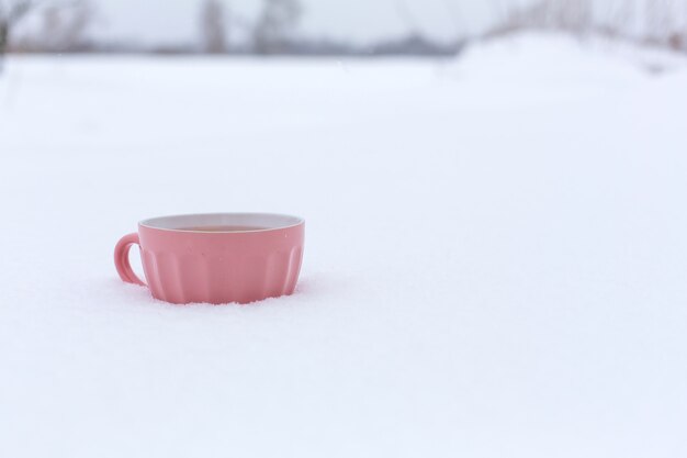 Uma caneca rosa com uma bebida está de pé na neve em uma rua no inverno