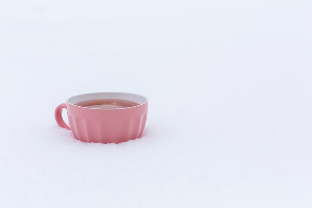 Uma caneca rosa com uma bebida está de pé na neve em uma rua no inverno