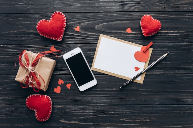 Uma carta de amor, corações de papel decorativos, presentes e smartphone em uma mesa escura