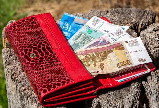 Uma carteira vermelha com notas russas nas denominações de 2000 1000 500 e 100 rublos encontra-se em um toco de madeira O conceito de poupança de investimento financeiro e dinheiro