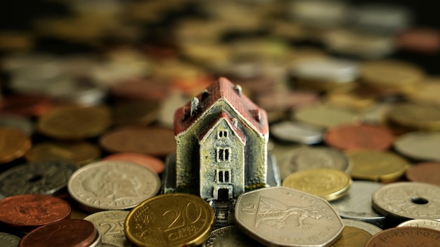 Uma casa com telhado vermelho fica em cima de uma pilha de moedas.