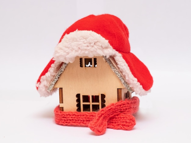 Uma casa de brinquedo de madeira na neve no inverno é coberta com um chapéu e enrolada em um lenço O conceito de se manter aquecido