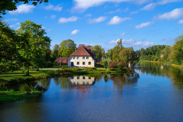 Uma casa de dois andares nas margens do Lago Jaunpils em um dia claro e ensolarado. Lindo gramado na frente de