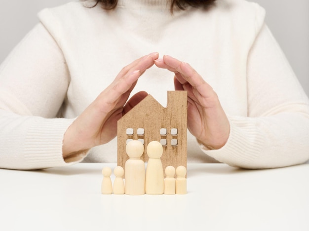 Uma casa de madeira e figuras de uma família, duas palmeiras femininas protegem objetos de cima. Conceito de seguro imobiliário, família feliz