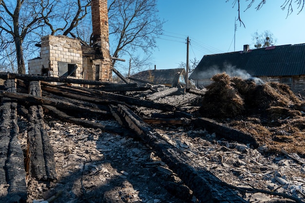 Uma casa de madeira na aldeia queimou por causa de um incêndio florestal Tábuas carbonizadas e várias coisas estão no chão cobertas de cinzas e fumaça