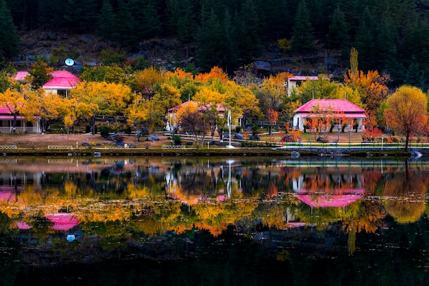 Uma casa na margem de um lago com telhado vermelho e árvores ao fundo.