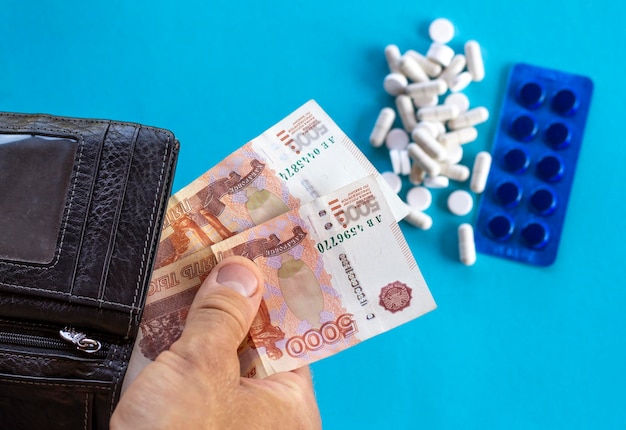 Uma cédula russa com um valor nominal de 5000 rublos na mão no contexto de um medicamento de pílulas em um fundo azul Conceito de custo de tratamento preço de medicamento orçamento de seguro de saúde