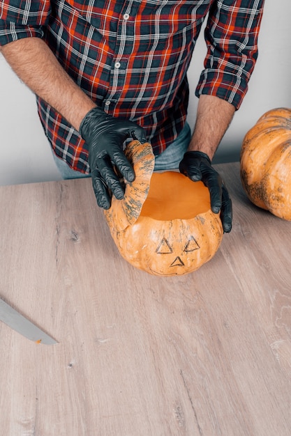 Uma cena vertical de uma pessoa usando luvas e esculpindo uma abóbora para o Halloween