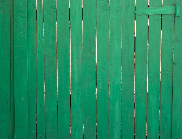 Uma cerca de madeira pintada com tinta verde. Há uma fechadura de porta em cima. As carteiras não são tão próximas umas das outras.