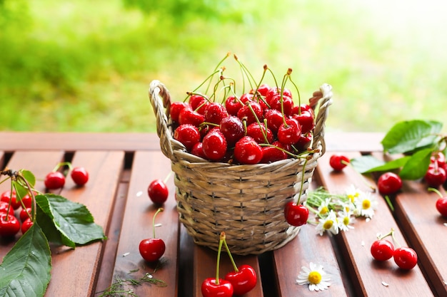 Uma cesta com frutas suculentas de vermelho em uma mesa de madeira na natureza de fundo com raios desfocados