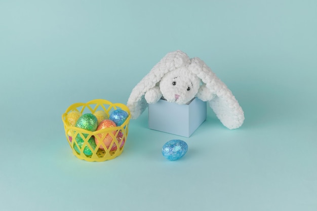 Uma cesta com ovos de páscoa coloridos e um coelho espreitando de uma caixa de presente. O conceito de Páscoa.
