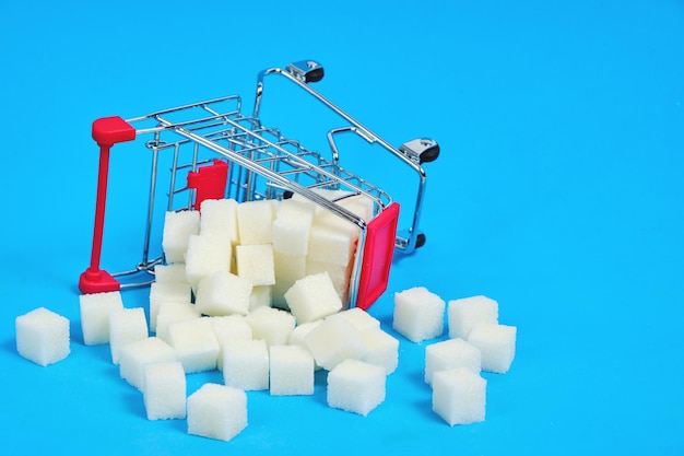 Uma cesta de compras virada com cubos de açúcar refinado espalhados em um fundo azul.