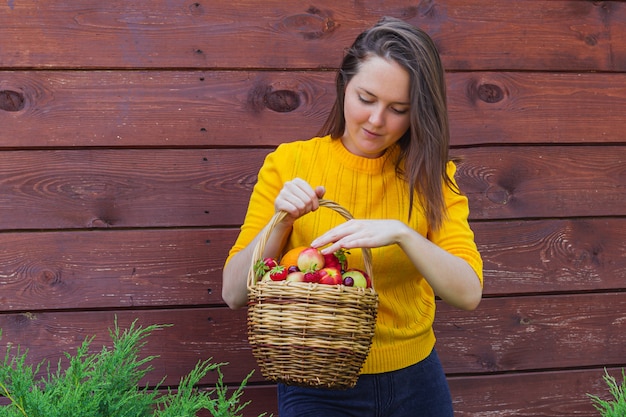 Uma cesta de vime com frutas frescas é segurada por uma jovem morena