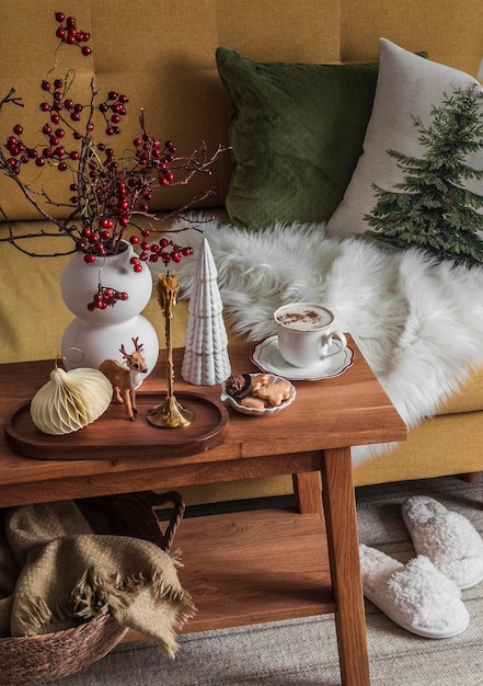Uma chávena de biscoitos cappuccino decoração de Natal em um banco de madeira perto do sofá com travesseiros no interior aconchegante da sala de estar pausa de café em casa