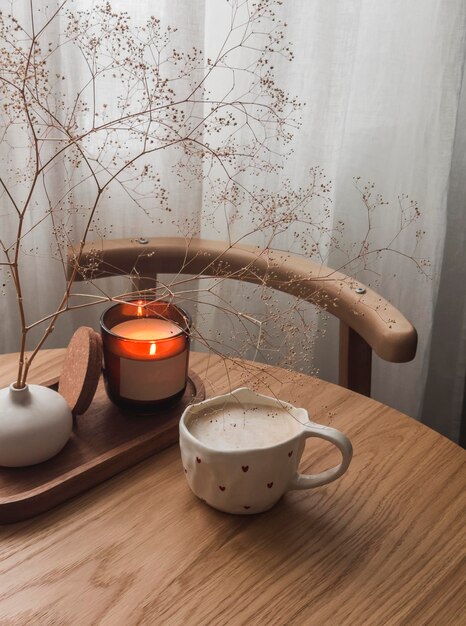 Uma chávena de cappuccino numa mesa redonda de madeira uma vela acesa uma aconchegante pausa para um café na sala de estar