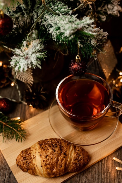 Uma chávena de chá com croissant perto da árvore de Natal. Véspera de Ano Novo em casa com a família.
