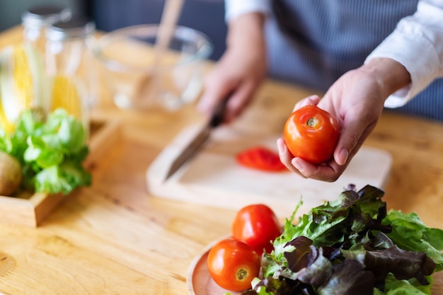 Uma chef segurando e colhendo um tomate fresco em uma bandeja de legumes sobre a mesa