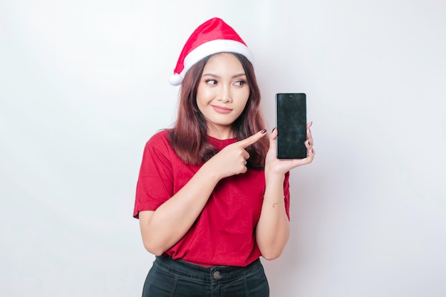 Uma chocada mulher de Papai Noel asiática está mostrando seu telefone isolado pelo conceito de Natal de fundo branco