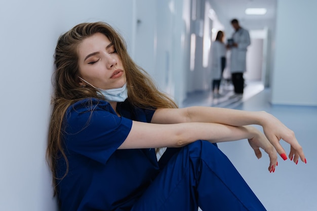 Uma cirurgiã está sentada no chão cansada após uma longa operação Enorme carga de trabalho dos hospitais durante a pandemia