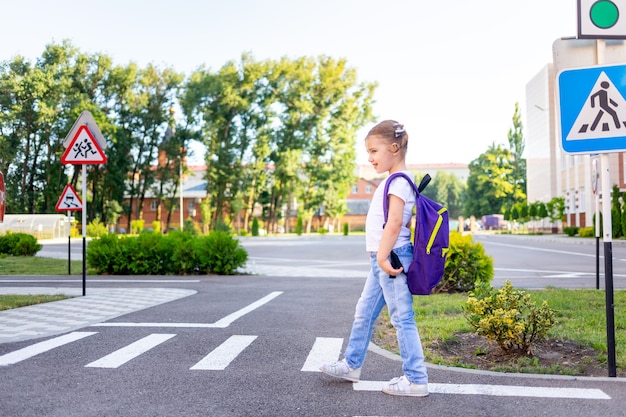 Uma colegial atravessa a estrada em uma zebra perto da placa de passagem de pedestres indo para a escola com uma mochila o conceito de regras de trânsito