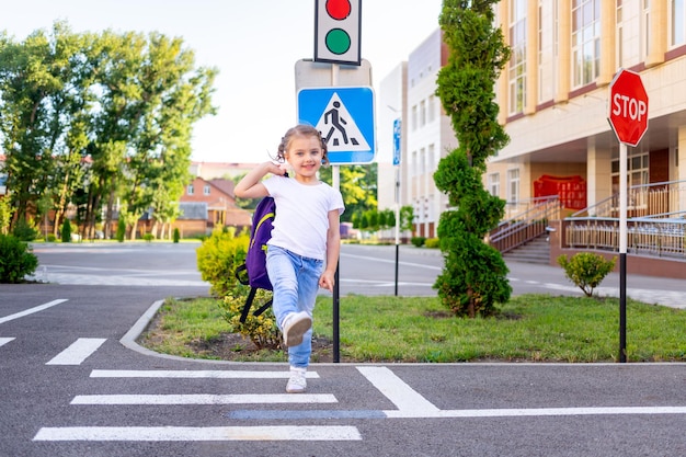 Foto uma colegial atravessa a estrada em uma zebra perto da placa de passagem de pedestres indo para a escola com uma mochila o conceito de regras de trânsito