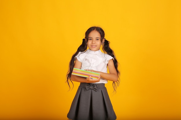 Uma colegial com cabelos escuros em um uniforme escolar cinza saia blusa branca com cadernos