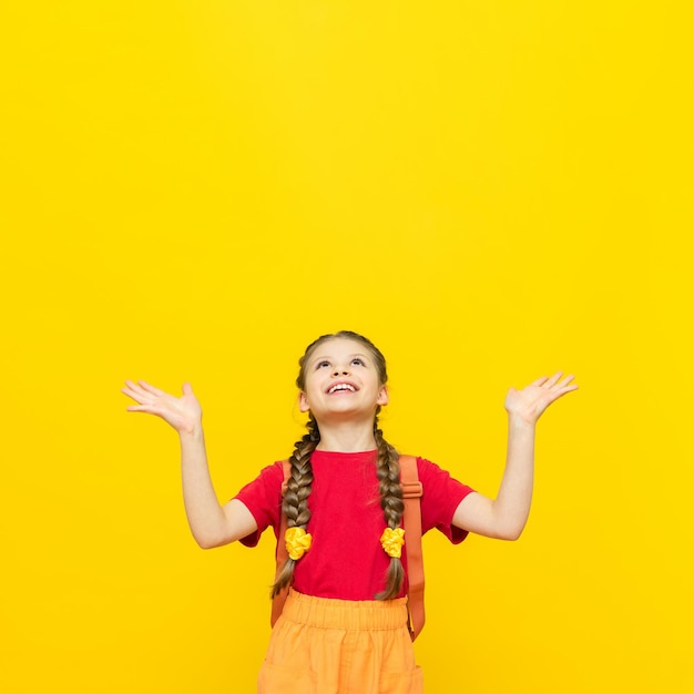 Uma colegial com uma mochila olha para o seu anúncio de cursos educacionais para crianças em idade escolar Uma garotinha está se preparando para os exames em um fundo amarelo isolado Copiar espaço