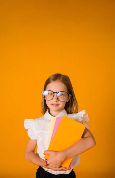 Uma colegial de uniforme e óculos segurando livros didáticos em um fundo amarelo