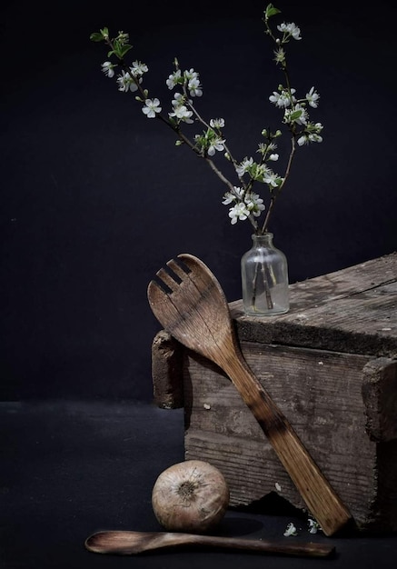 Uma colher de pau e uma garrafa de flores de cerejeira estão sobre uma mesa de madeira.