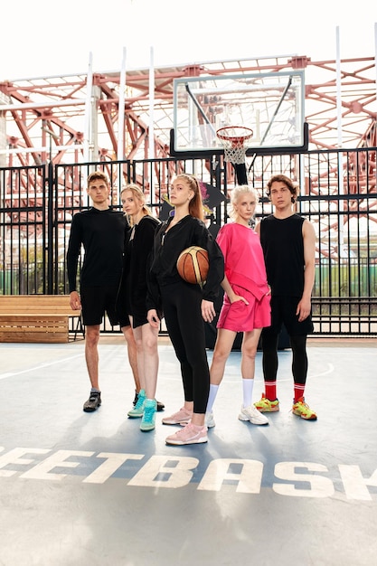 Uma companhia amigável de meninos e meninas está se divertindo na quadra de basquete, eles vão jogar basquete