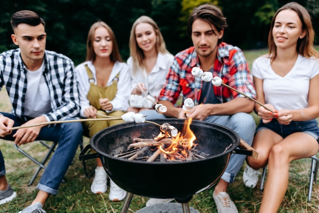 Uma companhia de amigos no acampamento cozinhando alimentos grelhados. Fundo desfocado