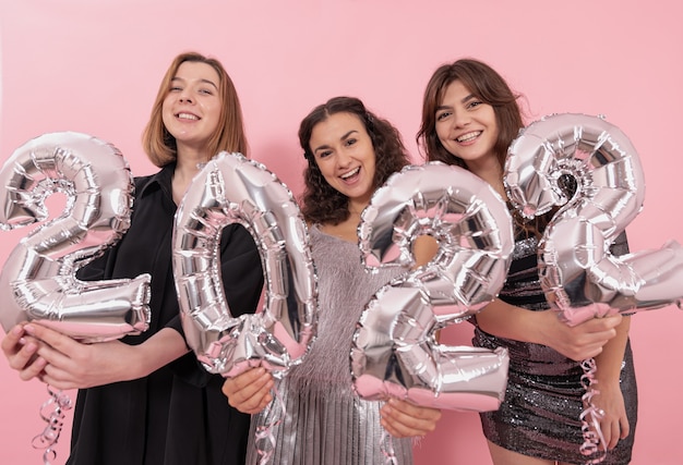Uma companhia de namoradas felizes em um fundo rosa com balões de folha de prata em forma de números 2022, comemorando o ano novo.